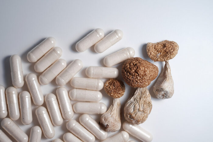 White pills and psilocybin mushrooms on white studio background, close up.